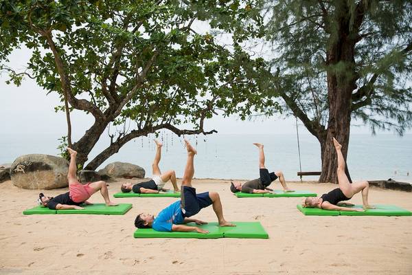 Mehrere Personen, die Yoga auf grünen Matten am Strand im Briza Beach Resort machen.