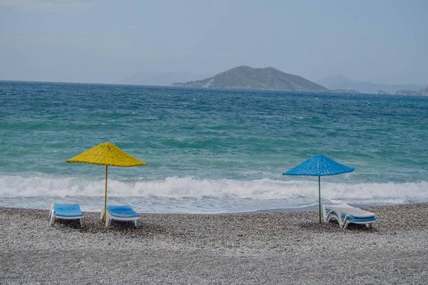 Strandszene am Malhun Hotel mit zwei Sonnenliegen und Sonnenschirmen, vor einem ruhigen Meer und einer kleinen Insel im Hintergrund.