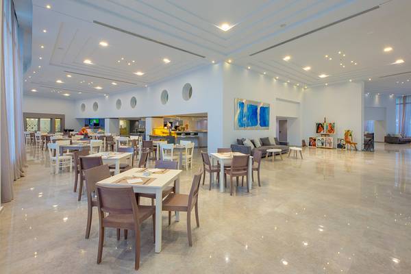 Restaurant im Akti Imperial Deluxe Resort & Spa mit weißen Tischen und Stühlen, Kunstwerken und einer Couch.
