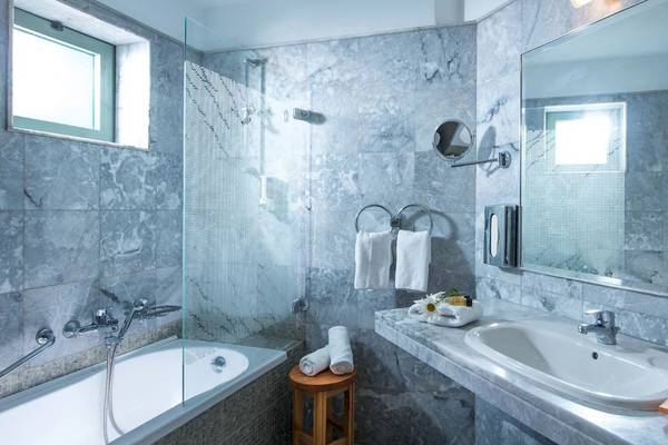 Ein Badezimmer im Bella Beach Hotel mit Marmorwänden, einer Badewanne, einem Waschbecken und Handtüchern.