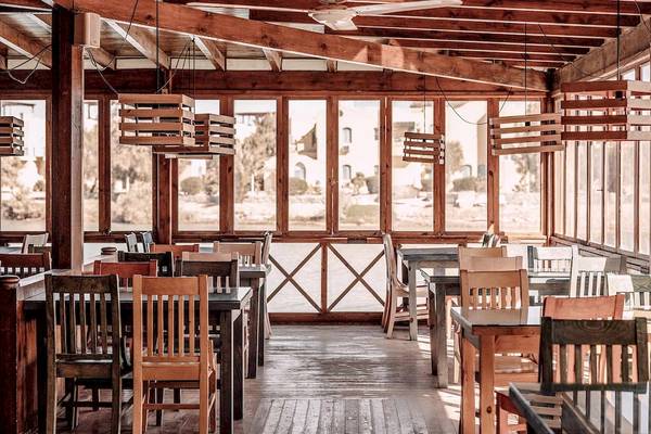 Innenansicht des Cook's Club El Gouna Restaurants mit Holztischen, Stühlen und großen Fenstern.