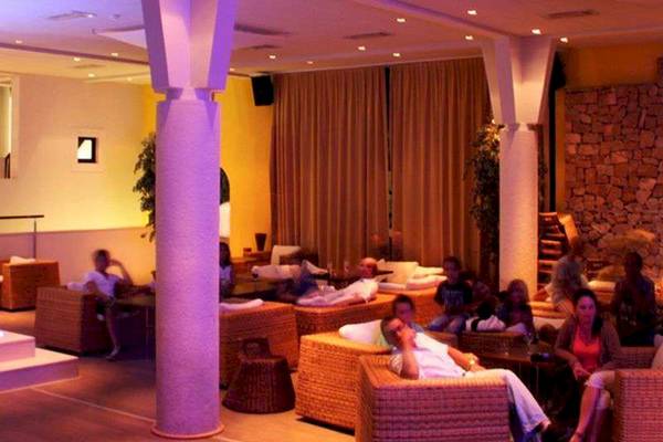Loungebereich im Bretanide Sport & Wellness Resort mit violetter Beleuchtung und vielen Gästen.
