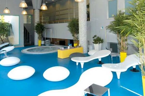 Innenbereich des Bretanide Sport & Wellness Resorts mit blauem Boden, weißen Liegestühlen, Pflanzen und einem Whirlpool.