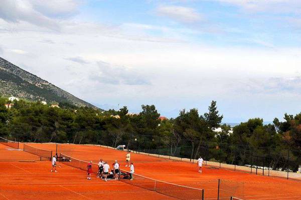 Tennisplatz im Bretanide Sport & Wellness Resort mit Spielern und Bäumen im Hintergrund.