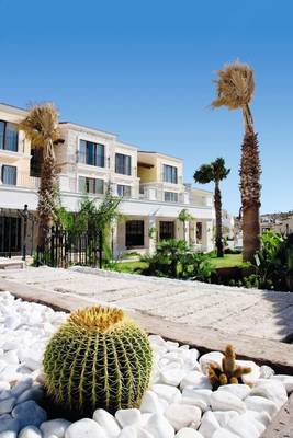Außenansicht des Cocos The Club Solto Hotels mit Palmen und Kakteen im Vordergrund.