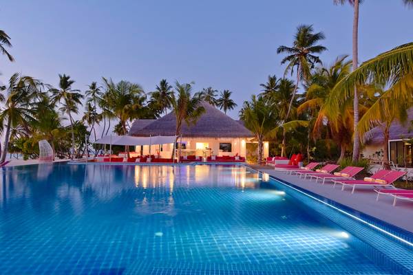 Außenpool mit Lounge-Sesseln und einer Bar im Hintergrund bei Nacht im Kandima Maldives