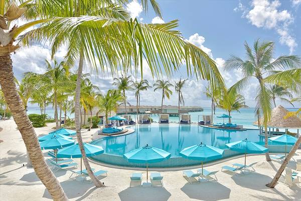 Poolbereich des Kandima Maldives mit blauen Sonnenschirmen und Liegestühlen am Strand