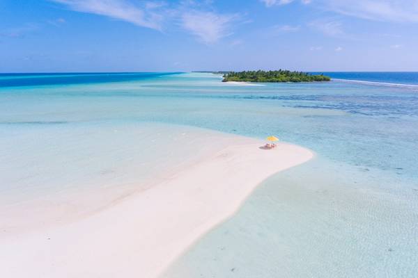 Luftaufnahme von Kandima Maldives mit einer kleinen Insel im Meer und einem Sonnenschirm auf dem Strand.