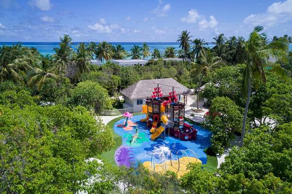 Ein Kinderspielplatz im Kandima Maldives Hotel mit bunten Spielgeräten und Meer im Hintergrund.