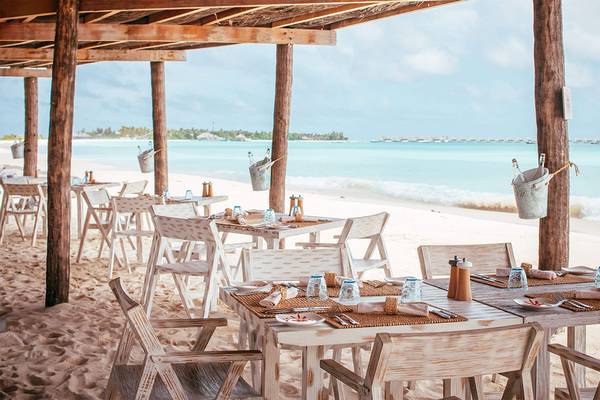 Ein Strandrestaurant auf dem Finolhu Baa Atoll in den Malediven mit weißen Tischen und Stühlen, die im Sand aufgestellt sind.