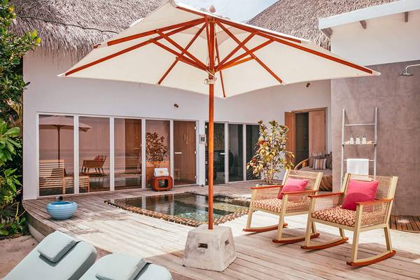 Außenbereich des Finolhu Baa Atoll Maldives Hotels mit Terrasse, weißem Sonnenschirm und zwei Sesseln.