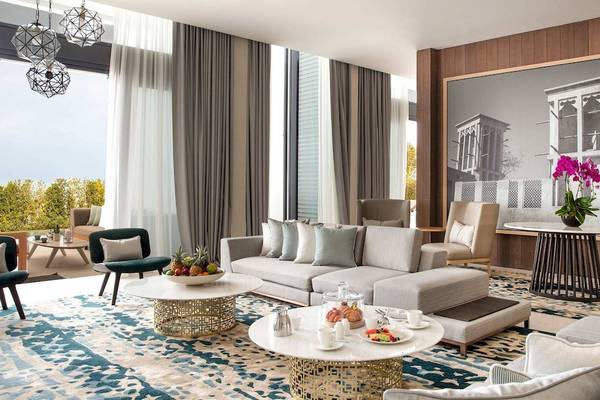 Wohnbereich des Jumeirah at Saadiyat Island Resort mit grauem Sofa, Tisch und Fenster mit Blick auf Bäume.