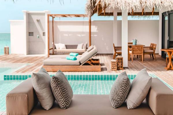 Loungebereich am Pool mit Sonnenliegen, Tisch und überdachter Veranda im Finolhu Baa Atoll Maldives Hotel.