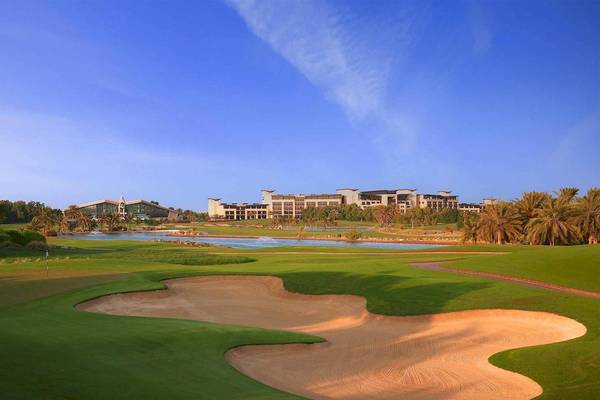 Golfplatz des Jumeirah at Saadiyat Island Resorts mit Wasserhindernis und Hotelgebäude im Hintergrund.