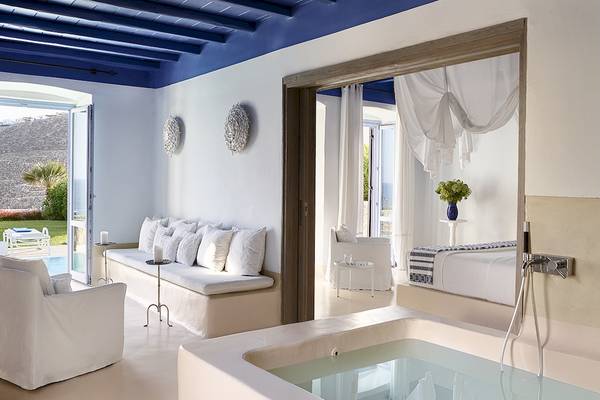 Innenansicht eines Zimmers im Grecotel Mykonos Blu Hotel mit Badewanne, Bett und offenem Fenster.