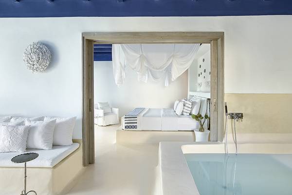Innenansicht eines Zimmers im Grecotel Mykonos Blu mit Badewanne, Bett und Sitzbereich.