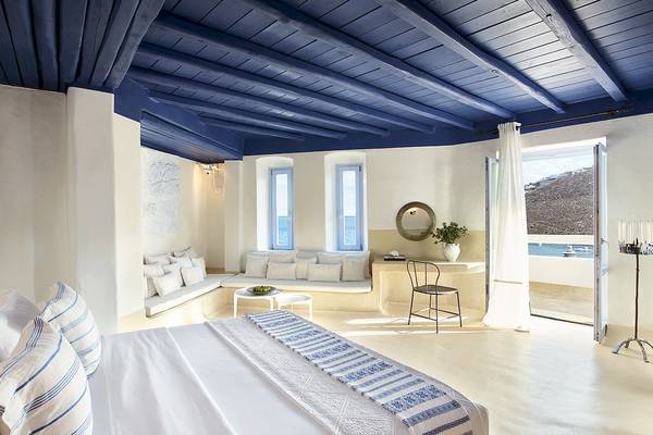 Innenansicht des Schlafzimmers im Grecotel Mykonos Blu mit blauer Decke, weißen Wänden und Meerblick.