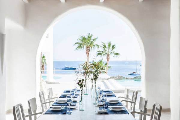 Speisetisch im Grecotel Mykonos Blu mit Blick auf das Meer und Palmen.