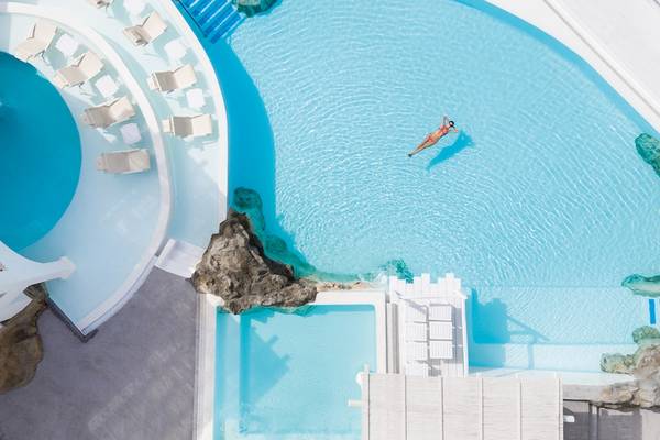 Luftaufnahme des Swimmingpools im Grecotel Mykonos Blu mit einer Person, die im Wasser schwimmt.