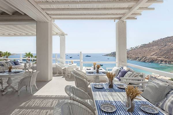 Terrasse des Grecotel Mykonos Blu mit Blick auf das Meer und eine Insel im Hintergrund.