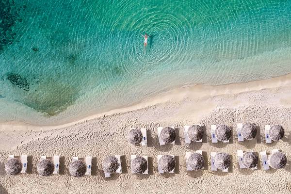 Luftaufnahme des Strandes des Grecotel Mykonos Blu Hotels mit einer Person im Wasser.