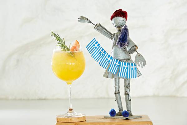 Ein Cocktailglas mit einem griechischen Dekofigure, die eine Flagge hält.