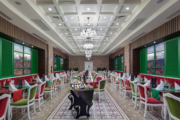 Innenansicht des Restaurants im Diamond Excellence Resort & Spa mit grünen und roten Stühlen, weißen Tischen und Kronleuchtern.