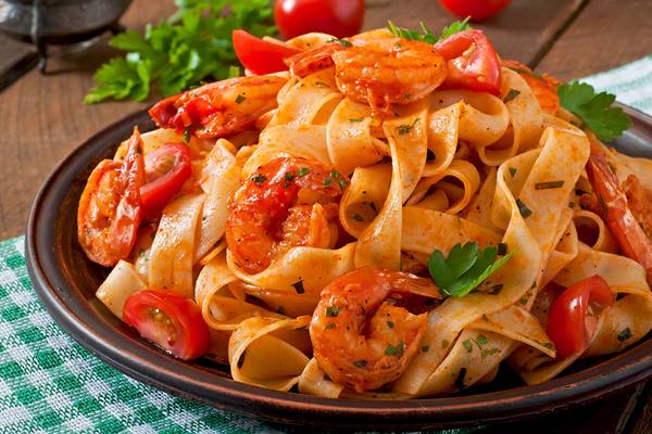 Ein Teller mit gebratenen Garnelen und Nudeln, garniert mit Tomaten und Petersilie.