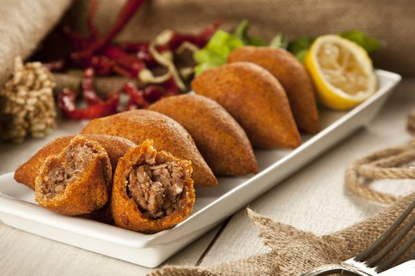 Orientalische Fleischspieße auf einem weißen Teller, begleitet von Salat und Paprika.