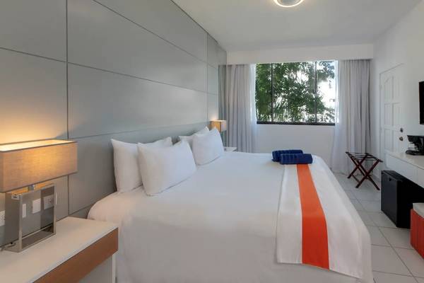 Viva Wyndham V Heavens Hotel Schlafzimmer mit großem Bett, weißen Wänden und Aussicht auf Bäume.