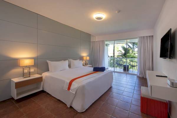 Innenansicht eines Hotelzimmers im Viva Wyndham V Heavens mit einem Bett, Balkon und Fernseher.