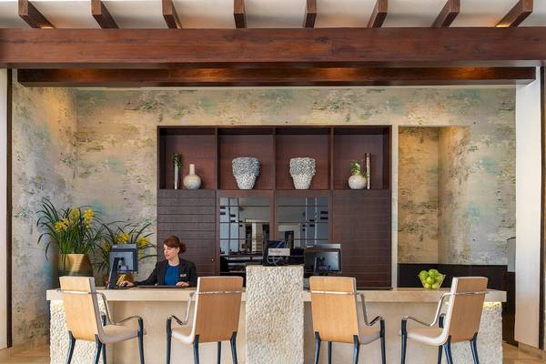 Empfangsbereich des H10 Estepona Palace Hotels mit Rezeptionistin, Vasen und Pflanzen im Hintergrund.