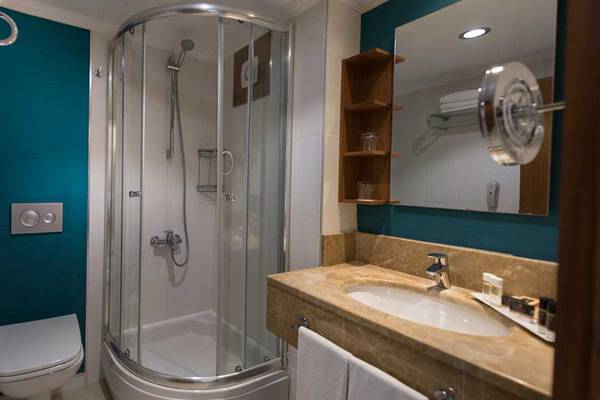 Badezimmer im Kamelya Aishen K Club Hotel mit Glasdusche, Waschbecken und Spiegel.