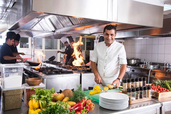 Ein Küchenchef im Kamelya Aishen K Club schneidet Gemüse, während seine Kollegen im Hintergrund kochen.