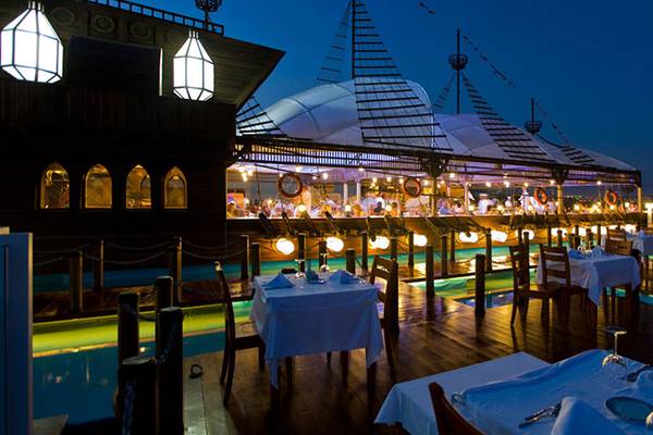 Abendaufnahme des Pool-Restaurants des Kamelya Aishen K Club mit illuminierten Tischen und Gästen.