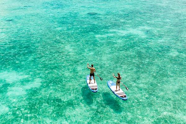 Zwei Personen auf SUP-Brettern im Meer, eines mit schwarzem und eines mit blauem Brett.