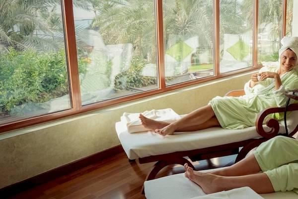 Zwei Frauen im grünen Bademantel sitzen in einem Hotel-Loungebereich mit Blick auf den See.