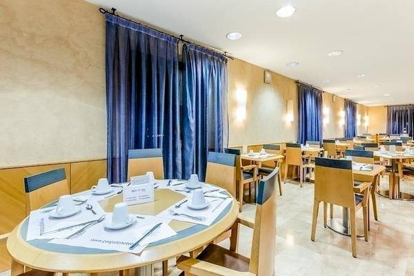 Frühstücksraum des Del Mar - Barcelona Hotels mit blauen Vorhängen und runden Tischen.