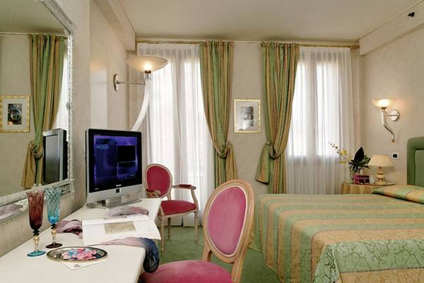 Innenansicht eines Zimmers im Principe Hotel Venedig mit einem Bett, Schreibtisch, Fernseher und Stühlen.