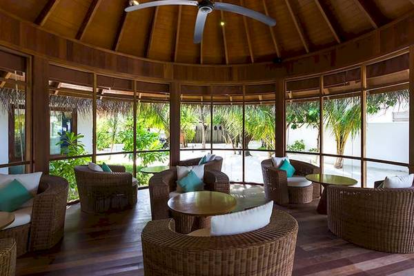 Loungebereich im Amaya Kuda Rah Hotel mit Korbsesseln, Tischen und Glaswänden.