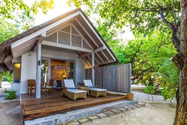 Foto eines Ferienhauses im Freien mit Sonnenliegen, Stühlen und einem Tisch auf einer Holzterrasse, umgeben von Bäumen.