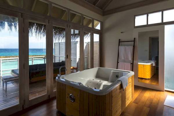 Ein Badezimmer mit einem Whirlpool im Freien, der an einen Balkon angrenzt, mit Blick auf das Meer und ein Sofa.