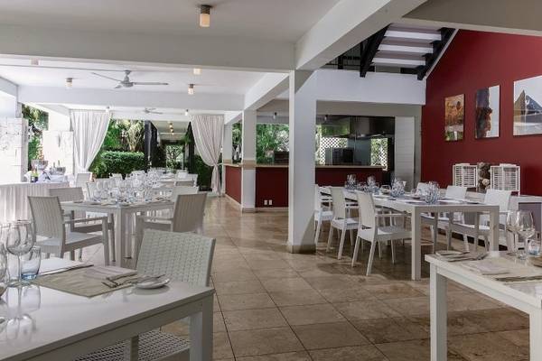 Innenbereich des Zoetry Curacao Resort & Spa Restaurants mit weißen Tischen und Stühlen, roter Wand und Bar.