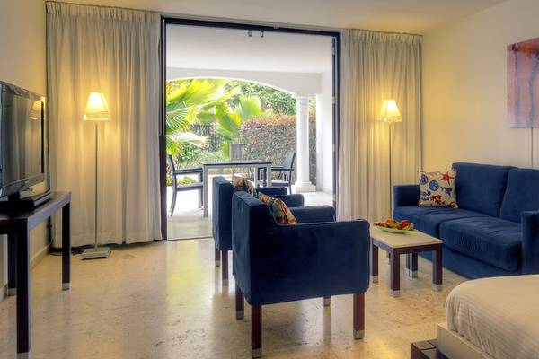 Wohnbereich im Zoetry Curacao Resort & Spa mit offenem Eingang, blauem Sofa und Tisch, Fernseher und Lampe.