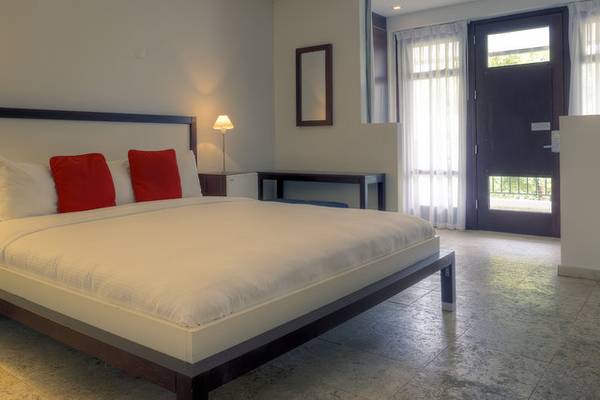 Ein modernes Schlafzimmer im Zoetry Curacao Resort & Spa mit einem weißen Bett, roten Kissen, und hellem Dekor.