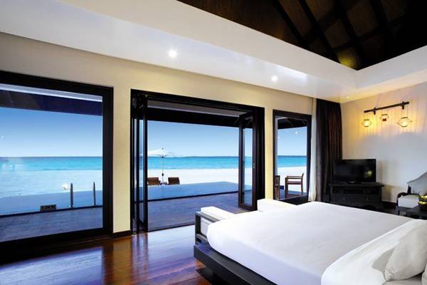Schlafzimmer im Atmosphere Kanifushi Maldives Hotel mit Blick auf das Meer und einen Balkon.