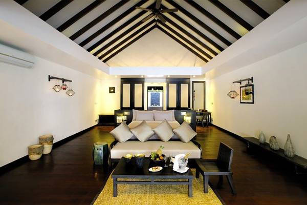 Schlafzimmer im Atmosphere Kanifushi Maldives Hotel mit Bett, Couch, Tisch und Dekor.