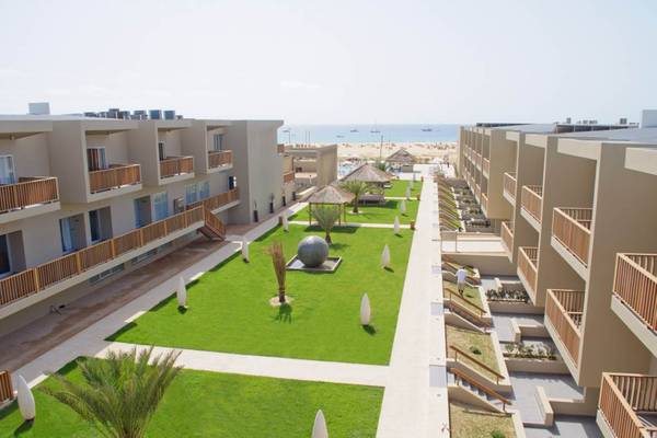 Außenansicht des Oasis Salinas Sea Hotels mit gepflegtem Rasen, Gebäuden und Meer im Hintergrund.