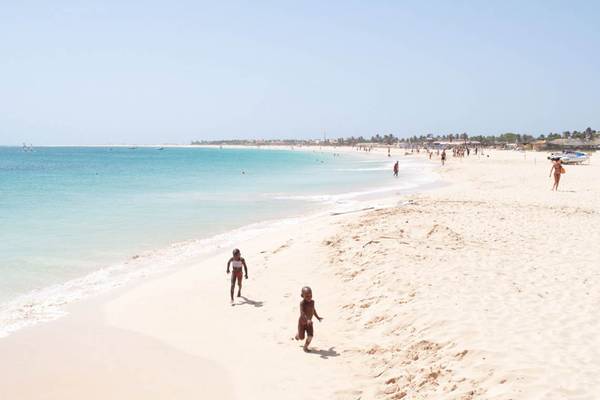 Ein Strand mit Kindern, die am Wasser spielen und im Hintergrund das Meer.