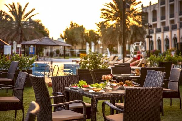 Gartensitzbereich im Al Ain Rotana Hotel mit Tischen, Stühlen und einem Swimmingpool im Hintergrund.